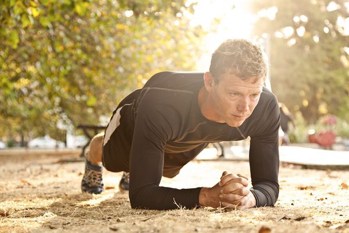 MAN EXERCISING IN PARK PERFORMING A PLANK