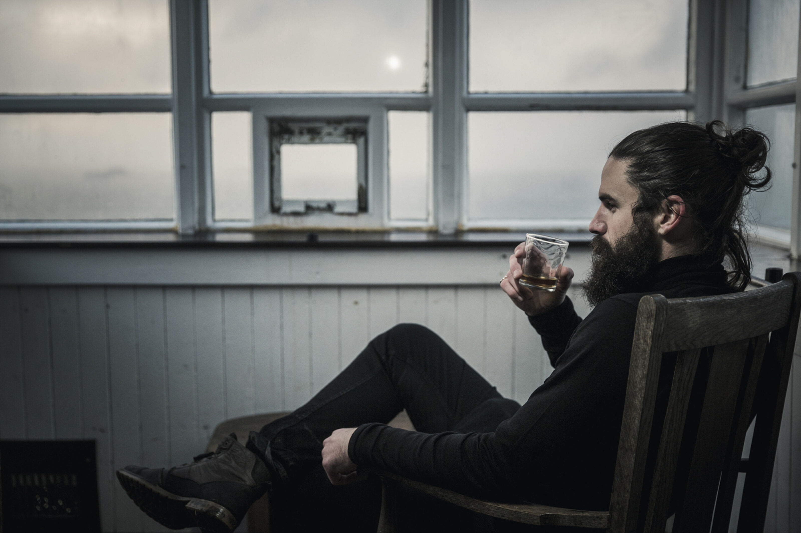 A man sitting looking at the view out of a window, drinking from a glass.
