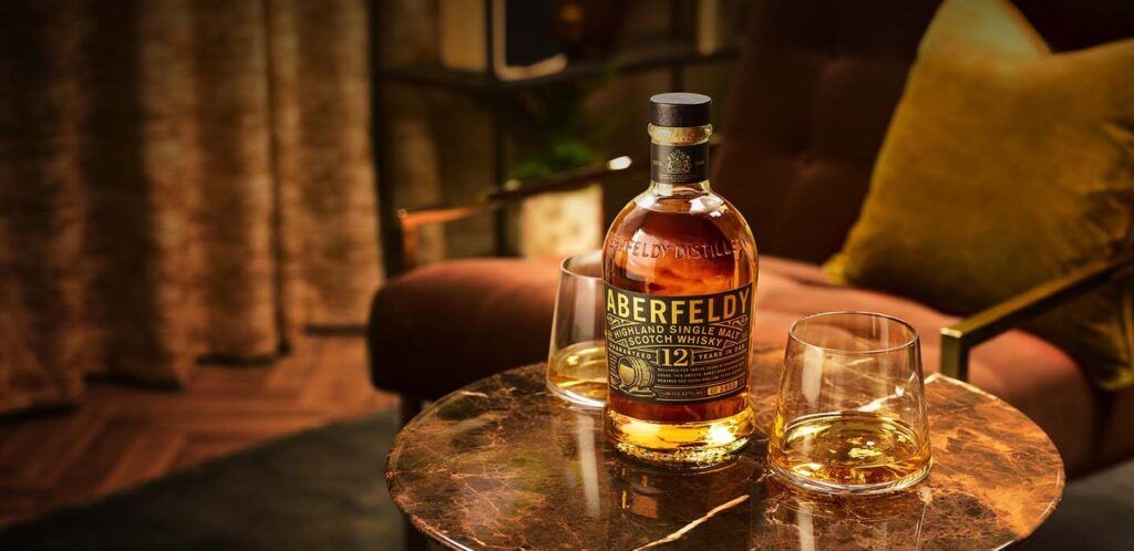 Aberfeldy Single Scotch Malt Whisky 12 Years Old neergezet op een tafel met twee halfvolle whiskyglazen.