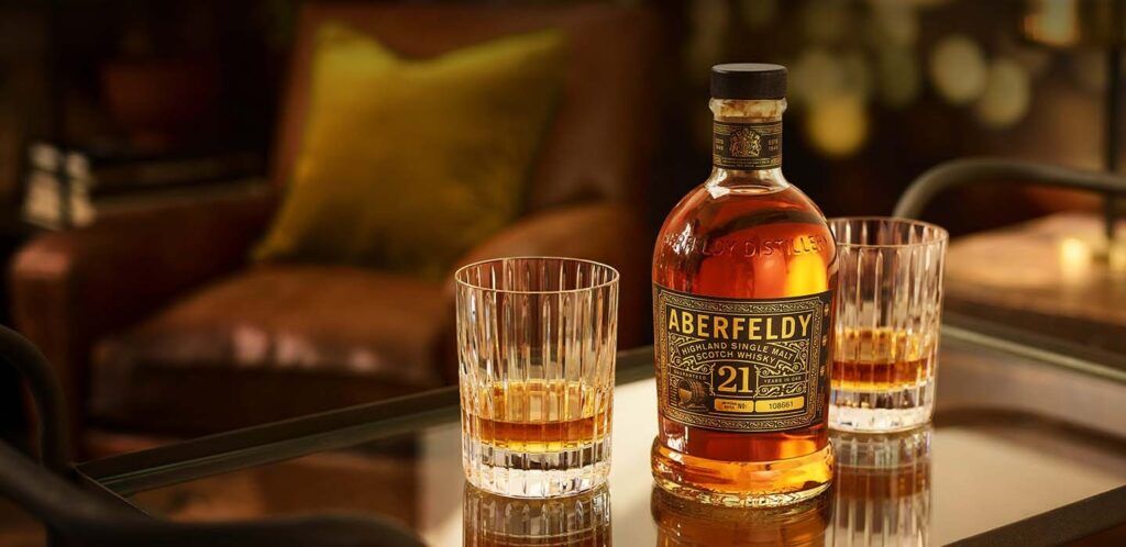 Aberfeldy Single Scotch Malt Whisky 21 Years Old neergezet op een tafel met twee halfvolle whiskyglazen.