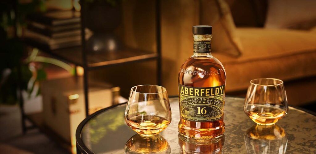 Aberfeldy Single Scotch Malt Whisky 16 Years Old neergezet op een tafel met twee halfvolle whiskyglazen.