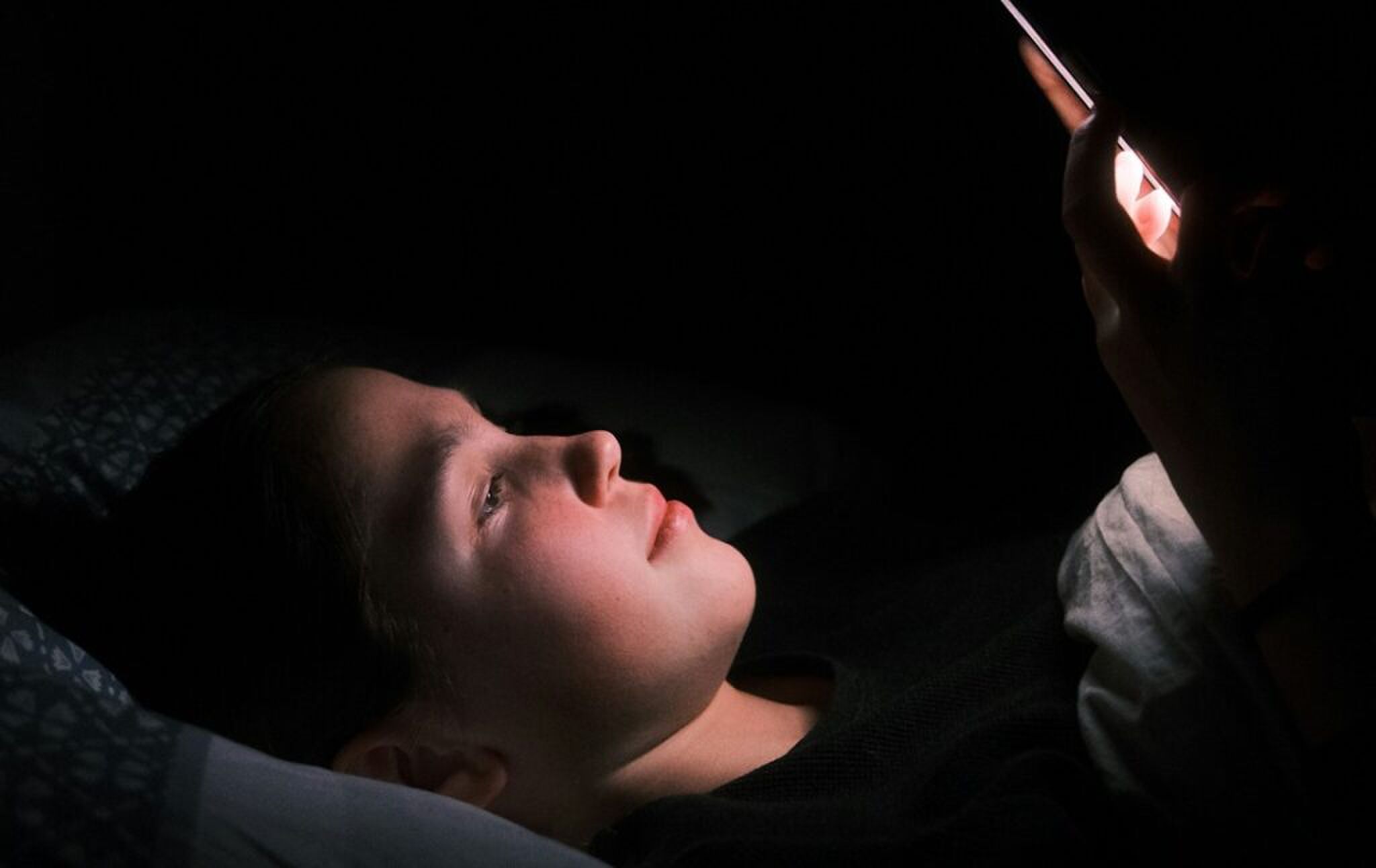 Een jongen die zijn belemmerd door blauw licht van zijn telefoon. 