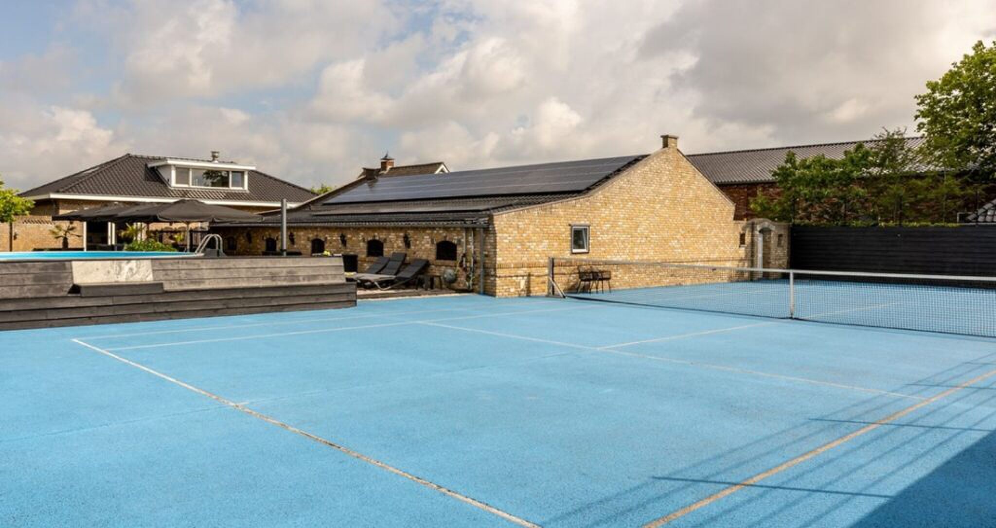 De felblauwe tennisbaan in de achtertuin.