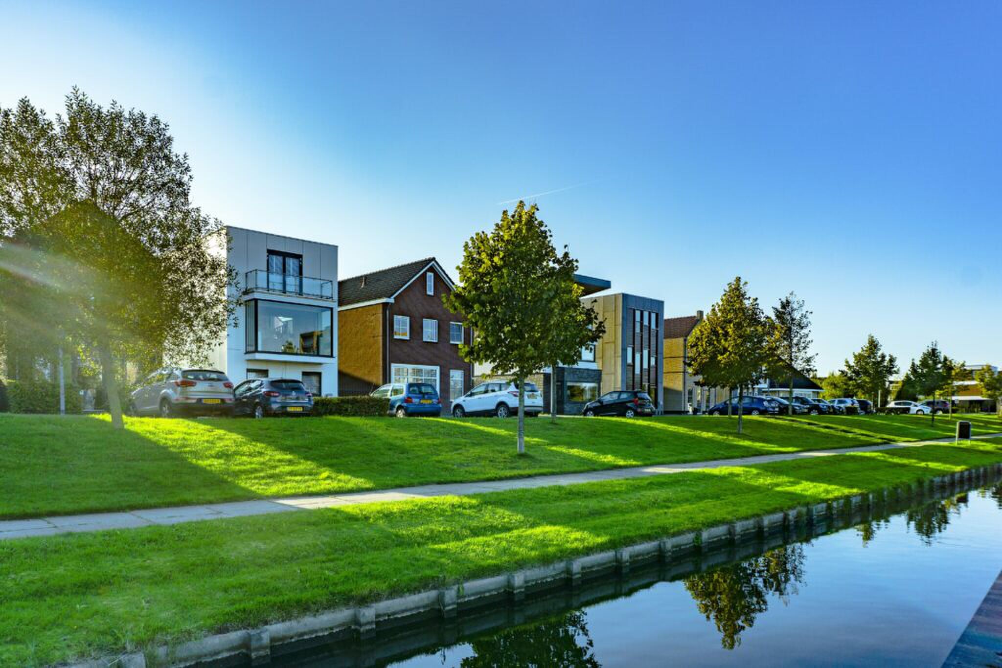 Een rij huizen met geparkeerde auto's langs een rivier
