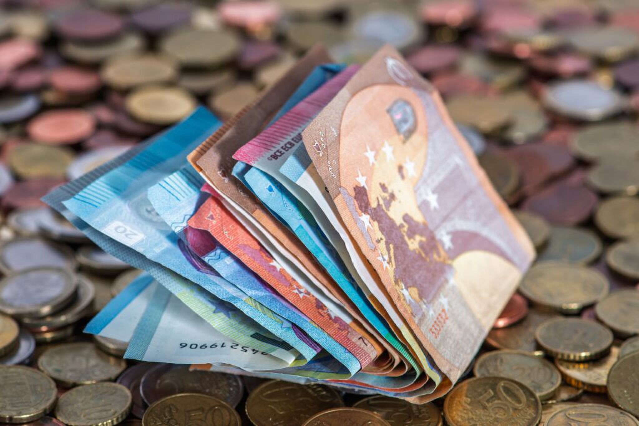 Een hele hoop gevouwen briefjes geld, opgestapeld op een hoop muntgeld (dit verschil zal de koopkracht in 2026 niet zijn)