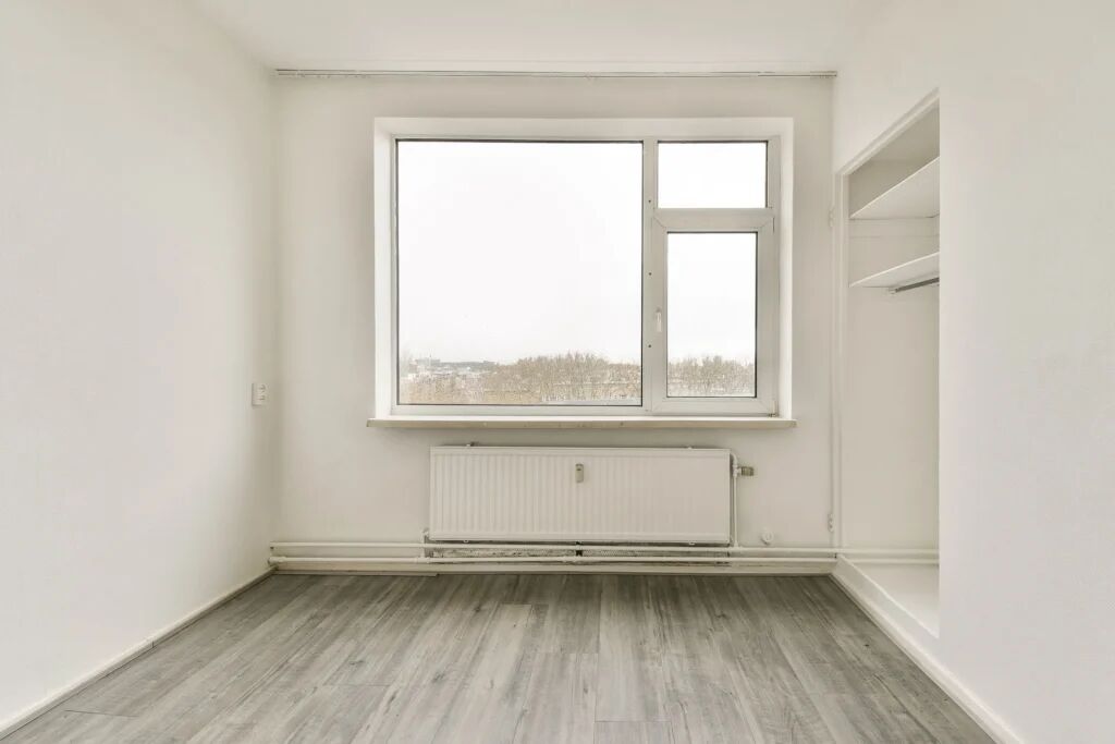 Een leeg appartement met een raam en verwarming.