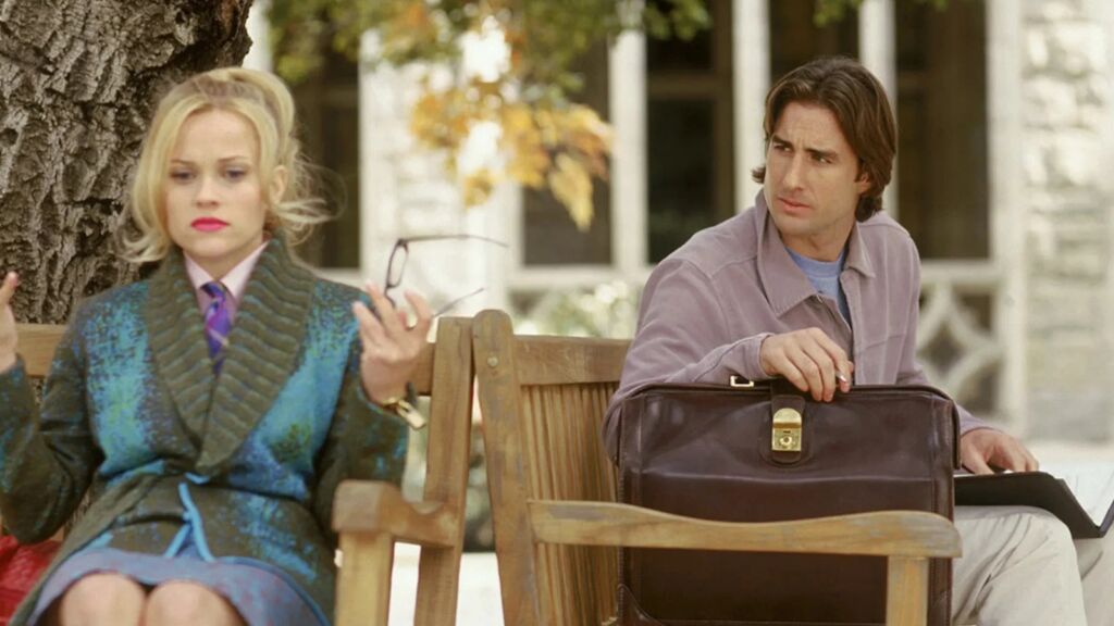 Een vrouw die boos op een bankje zit, met daarachter een man op een bankje die naar haar kijkt. 