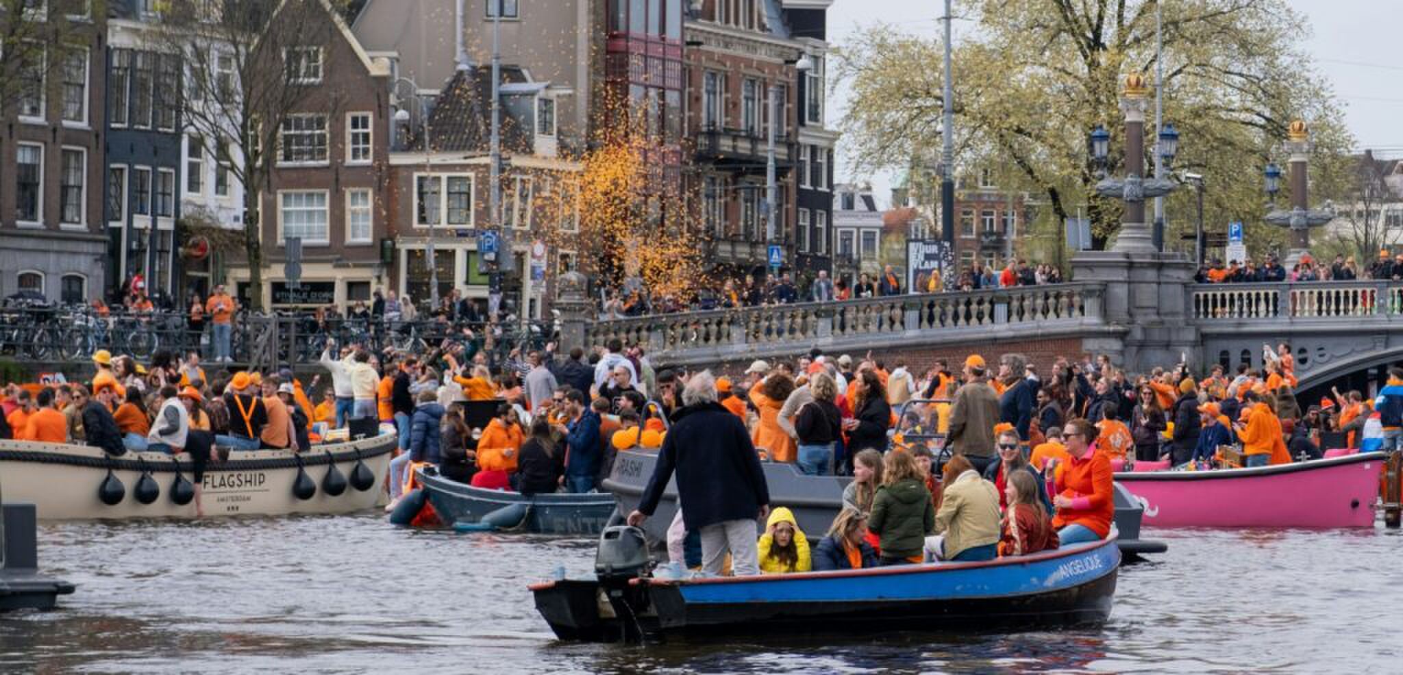 De Amsterdamse grachten met bootjes met mensen die oranje dragen. 