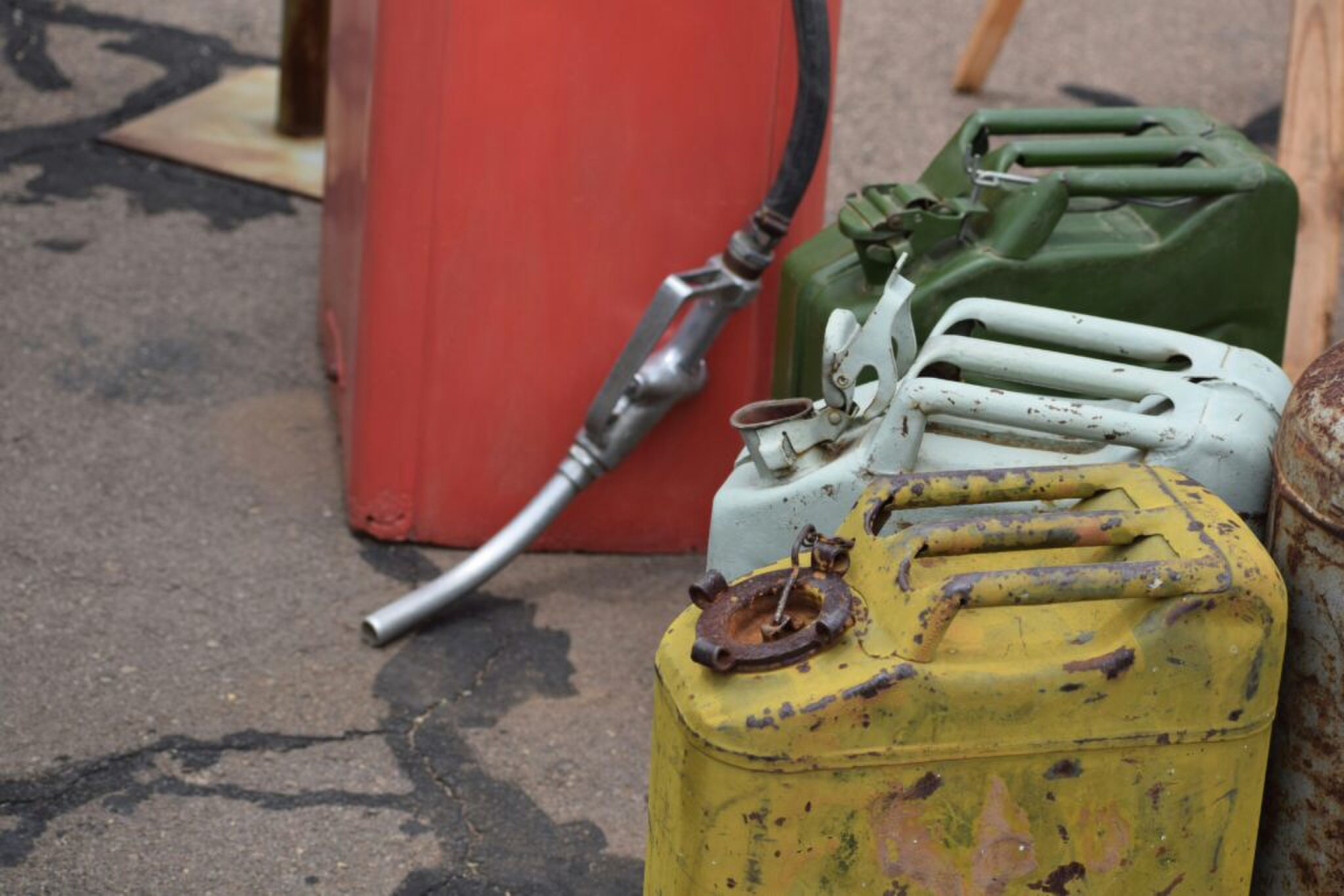 3 oude, gekleurde jerrycans naast een benzinepomp