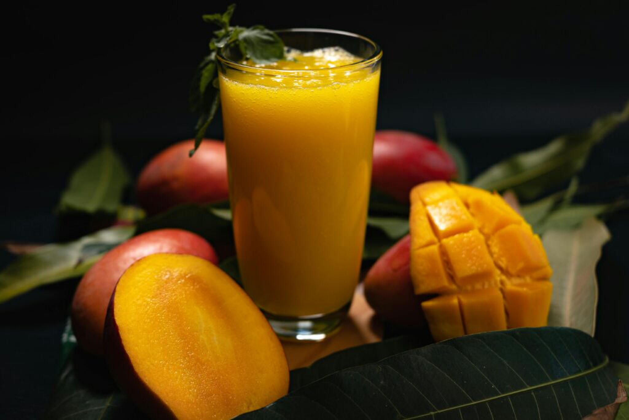 Een glas met vruchtensap met mango's eromheen.