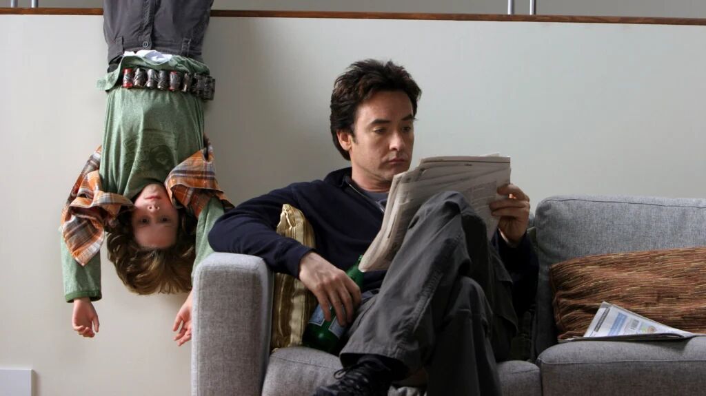 Een vader die de krant zit te lezen en zijn kind die ernaast hangt op z'n kop. 