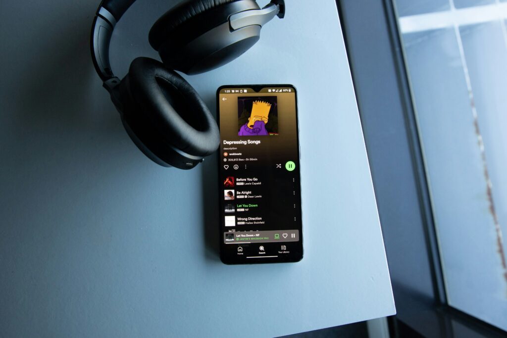 Een telefoon met spotify en een koptelefoon ernaast.