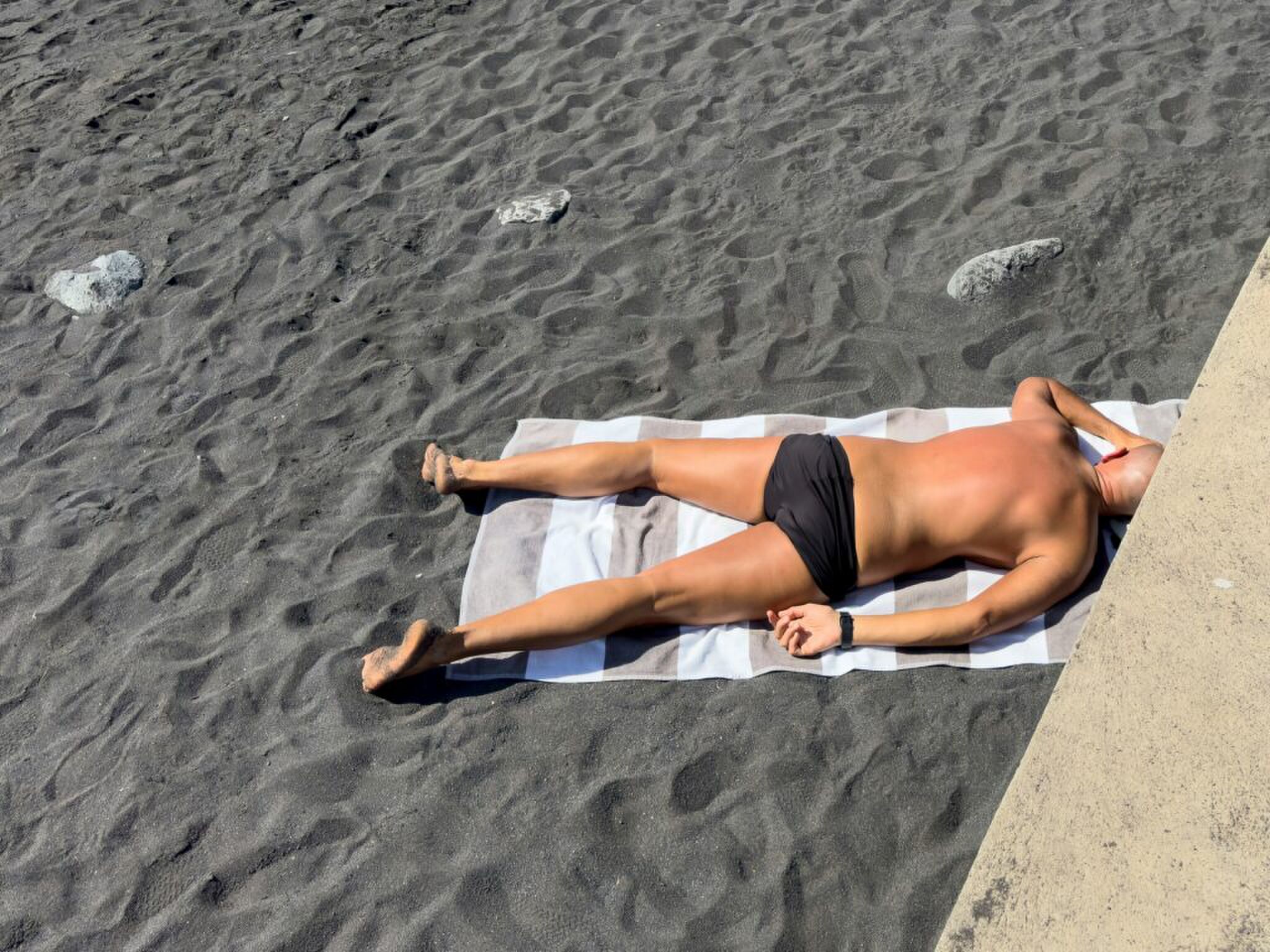 Een man die op zijn buik op het strand ligt.