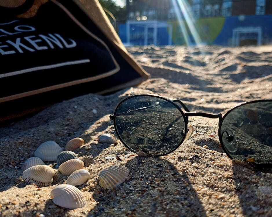 Een zonnebril in het zand. De zonnestralen vallen op de achtergrond