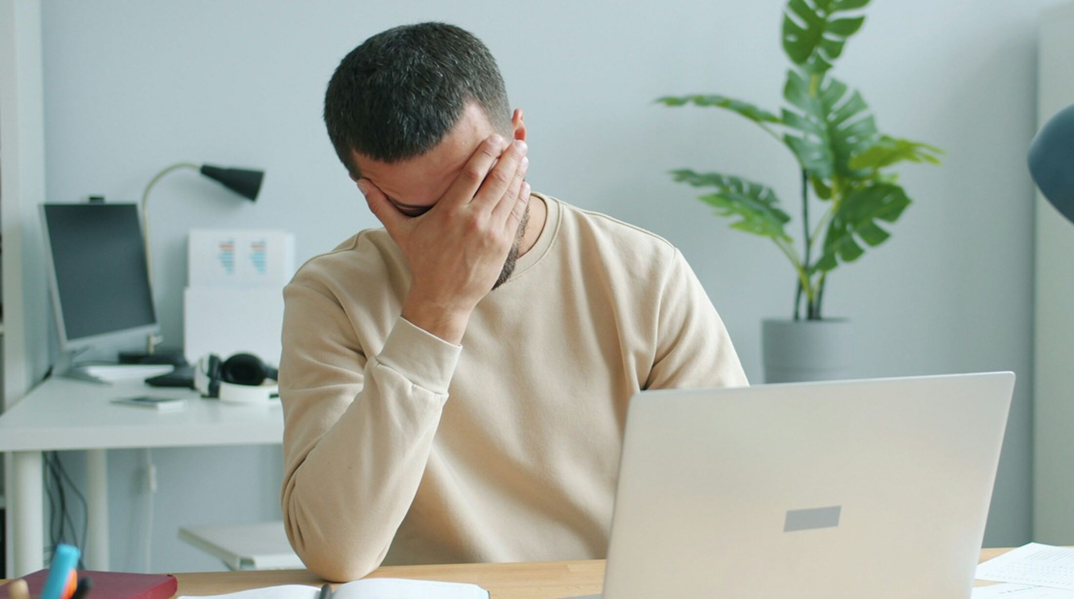 Man achter een laptop met hand voor het hoofd.