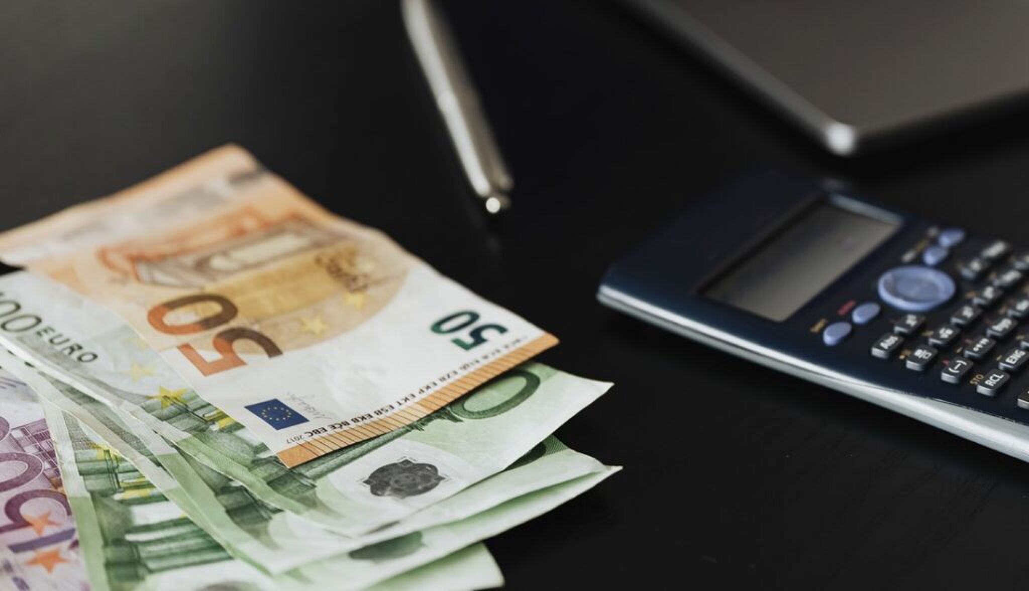 Een rekenmachine en cashgeld op een zwarte tafel.