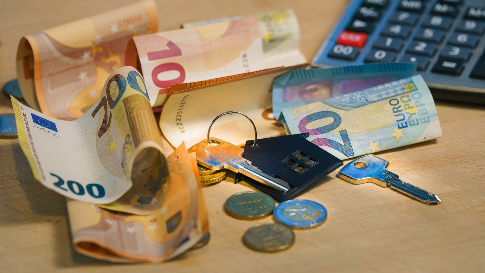 Geld dat op tafel ligt met een rekenmachine en sleutel.