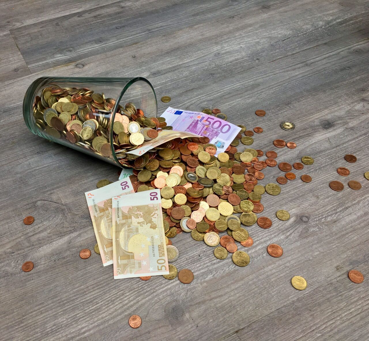 Een glas dat is gevallen met allemaal muntjes die eruit vallen.
