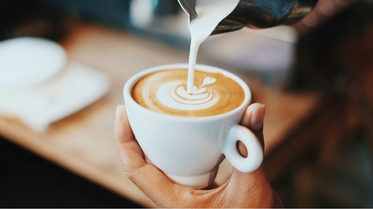Iemand die melk schenkt in een kopje koffie. 