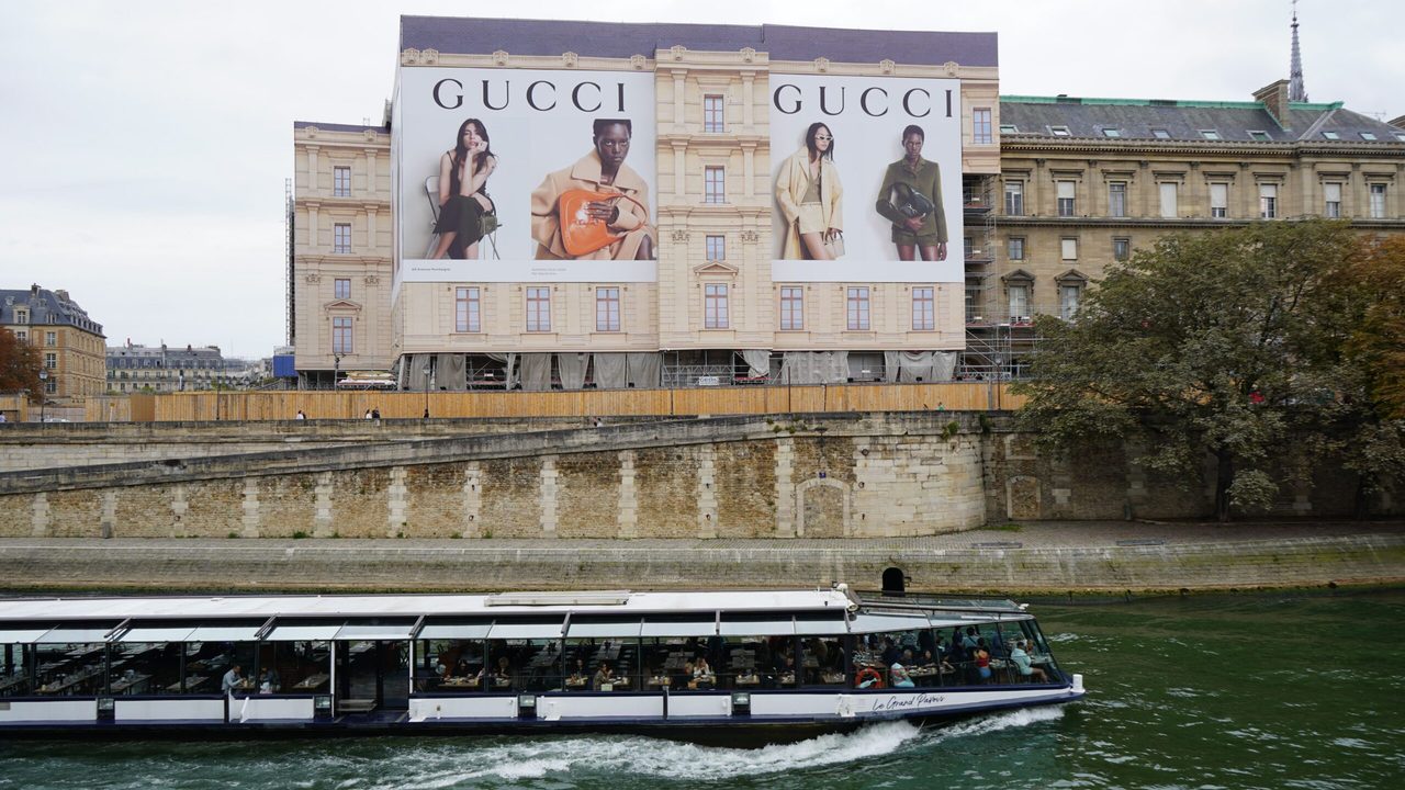 Een Gucci reclamebord langs de Seine in Parijs met een passerende cruiseboot.