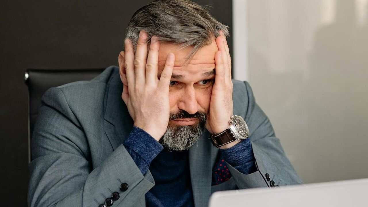 Man die met hoofdpijn voor zijn laptop zit omdat hij de dag ervoor veel alcohol heeft gedronken, wat zijn levensduur verkort