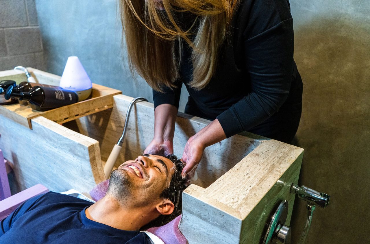 Een vrouw die een man zijn haar wast met shampoo.