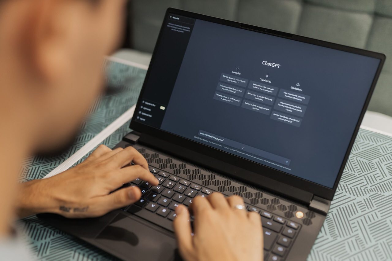 Iemand die achter zijn laptop zit met ChatGPT op het beeldscherm. 