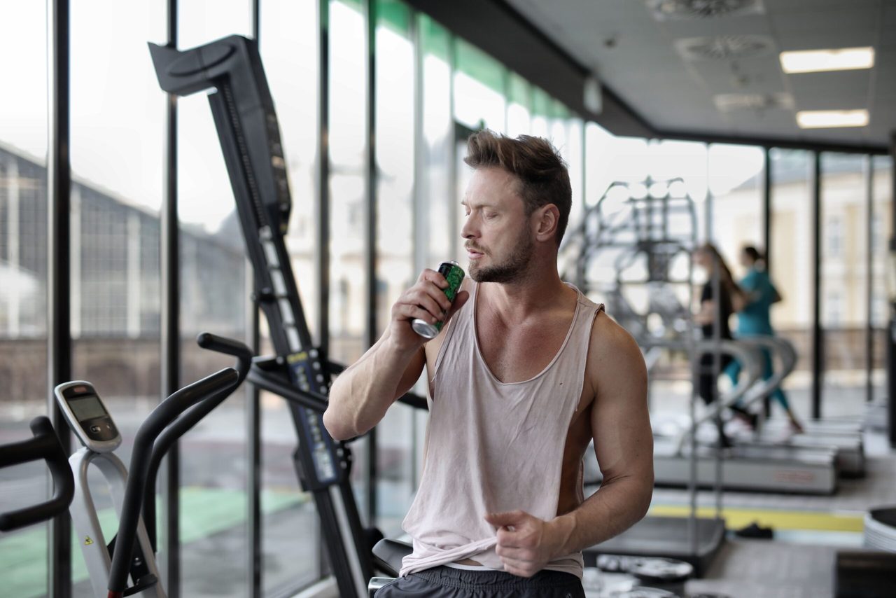 Een man die een sportdrnakje drinkt in de sportschool. 