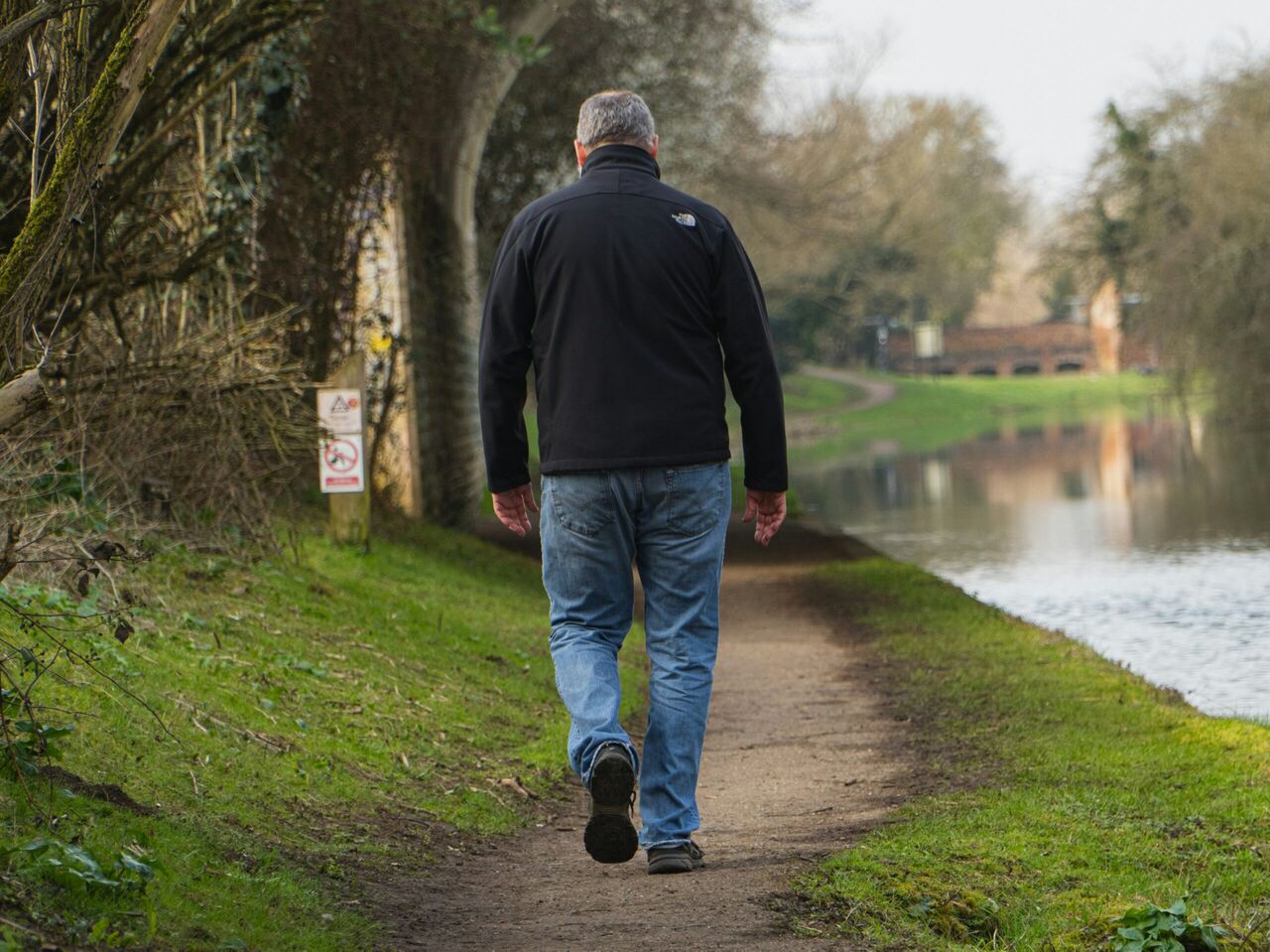 Een man die wandelt op een pad langs het water.