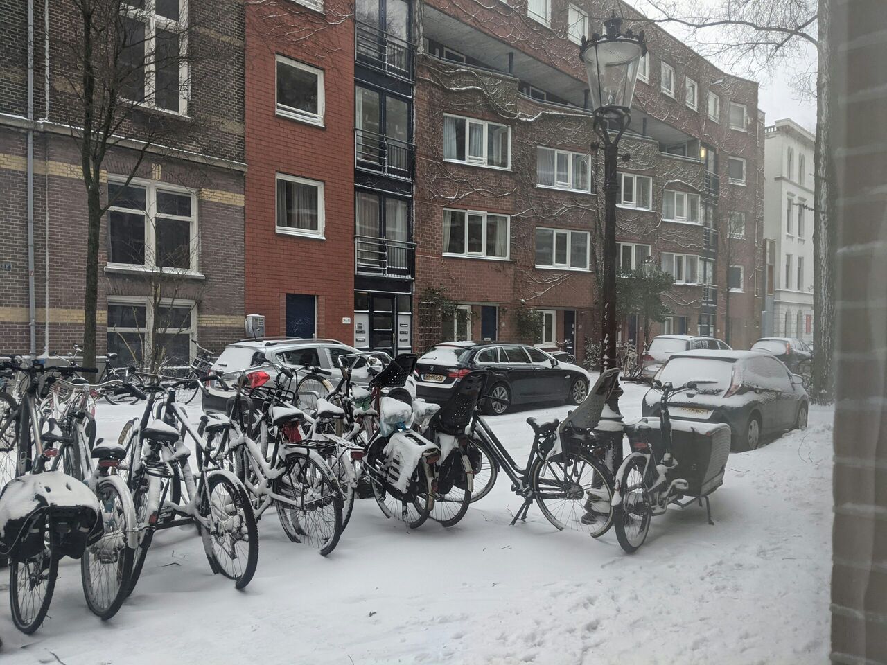 Een weg met geparkeerde auto's en fietsen ondergesneeuwd 