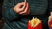 Een persoon die de dag na Koningsdag frietjes van de McDonald's eet