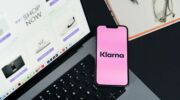 Telefoon met het Klarna-logo naast een laptop met een open online webshop, illustratie van achteraf betalen