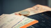 Twee vliegtickets liggen naast een euromunt en een biljet van 50 euro op een tafel