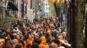 Een straat die versiert is voor Koningsdag en mensen die veel oranje dragen.