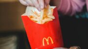 Iemand die frietjes pakt uit een McDonald's-verpakking.