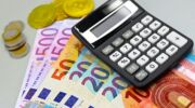Een hele hoop geld (zowel brief- als muntgeld) naast een rekenmachine