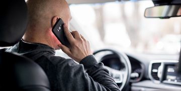 Een man die niet handsfree aan het bellen is en zo een boete kan verwachten