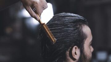 Een man die zit en iemand die zijn haar kamt.