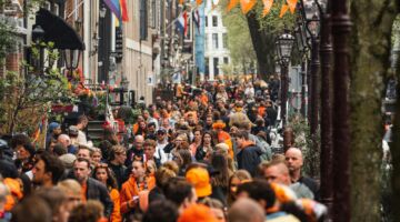 Een straat die versiert is voor Koningsdag en mensen die veel oranje dragen.