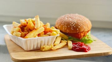 Een patatje en een hamburger die op een plank liggen.