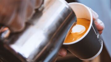 Iemand die melk schenkt in een kopje koffie.