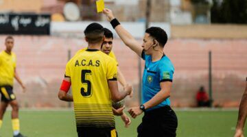 Een scheidsrechter die een gele kaart uitdeelt, die resulteert in een boete voor de speler