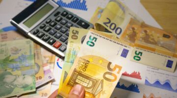 Iemand die geld in z'n hand heeft en op de tafel ligt nog meer geld en een rekenmachine.