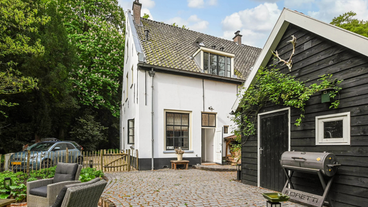 Een wit huis met een zwarte schuur ernaast.