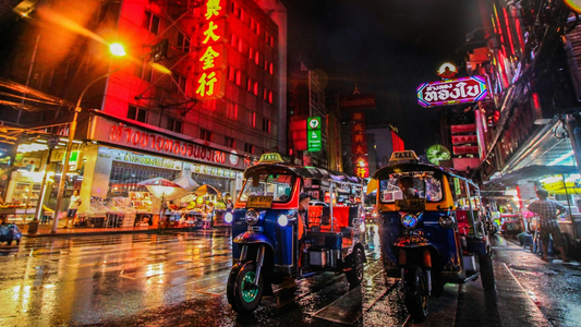 Een straat in Bangkok met veel neonlampen en tuktuks.