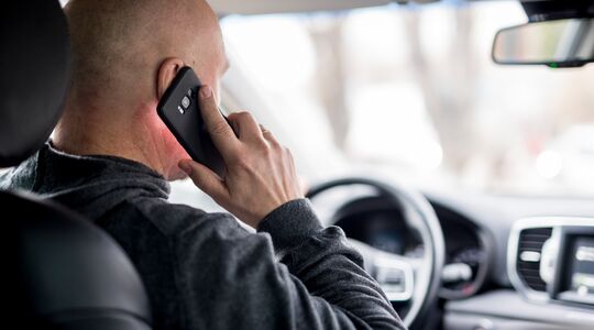 Een man die niet handsfree aan het bellen is en zo een boete kan verwachten