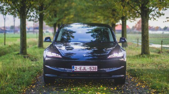 Een Tesla Model 3 rijdt over een bosweg