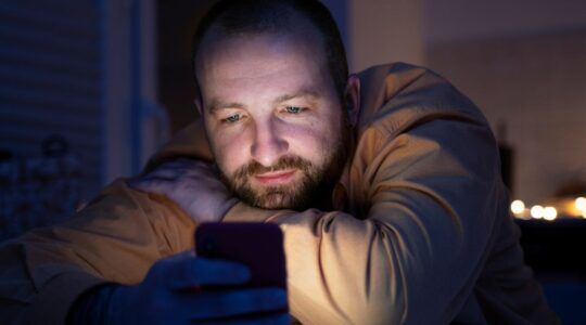 Man die in bed ligt met zijn telefoon met veel blauw licht, dat slecht zou zijn voor je slaap