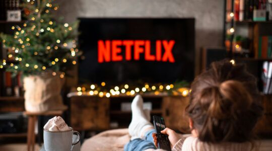 Een vrouw ligt op de bank, afstandsbediening in hand en kijkt Netflix