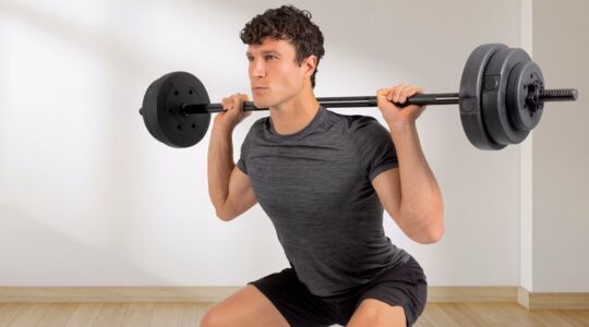 Een man doet een squat met de halterstangset van de ALDI